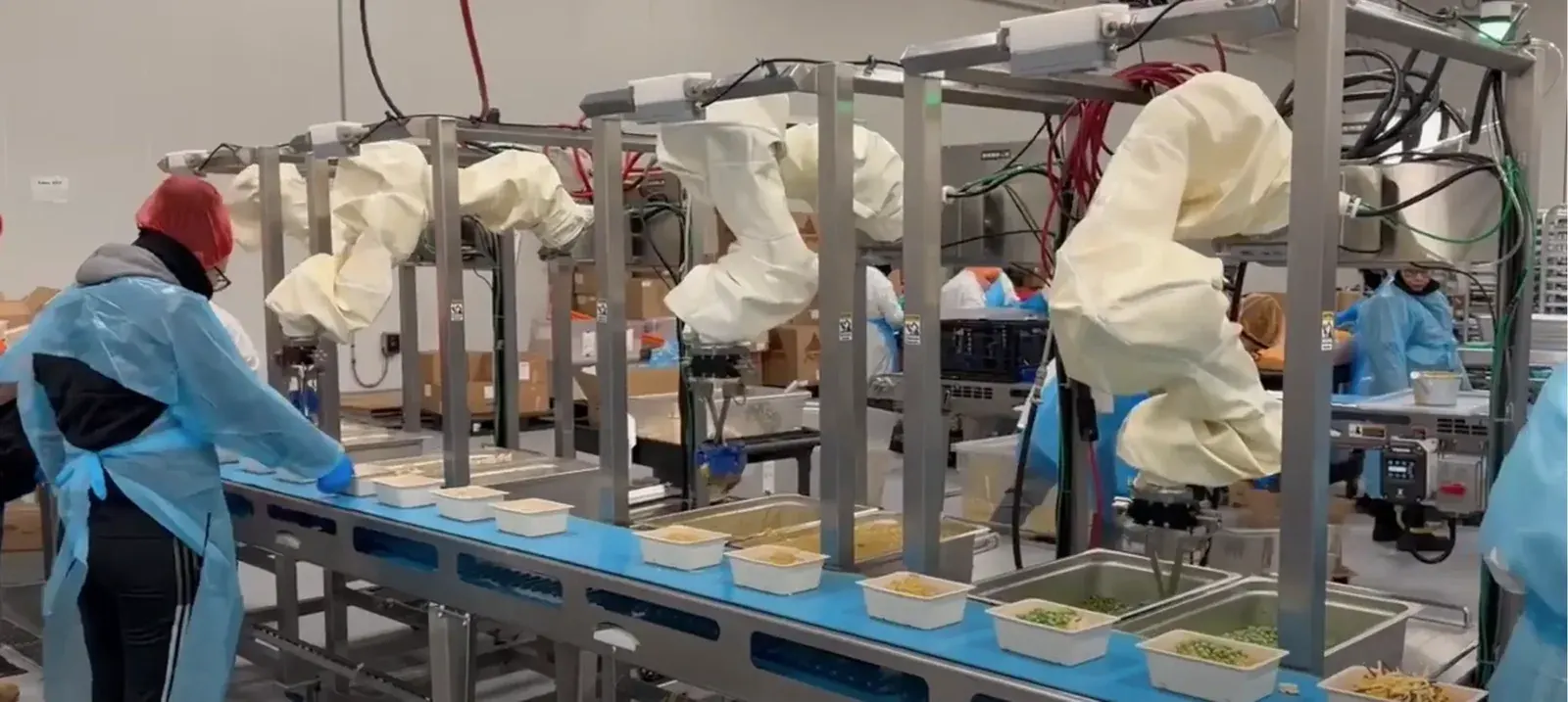 Chef Robotics arms working a live food production line beside gowned workers
